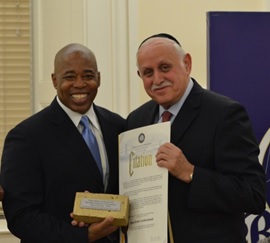 Brooklyn Borough President Eric Adams (left) presents Dr. Robert Goldschmidt, executive dean of the Lander College of Arts and Sciences in Flatbush and Touro’s vice president for planning and assessment, with a citation and gold-plated cornerstone brick, symbolizing his numerous contributions to the community and to the building of “One Brooklyn.”  