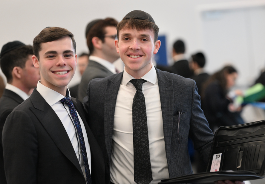 Two male students smile dressed in suits smile at the annual Touro career fair.